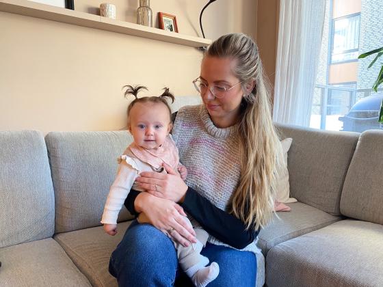 En kvinne sitter i sofaen med et barn p&aring; fanget. Barnet smiler