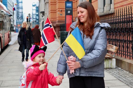 mor og datter p&aring; et fortau som holder det norske og det ukrainske flagget i kryss og smiler