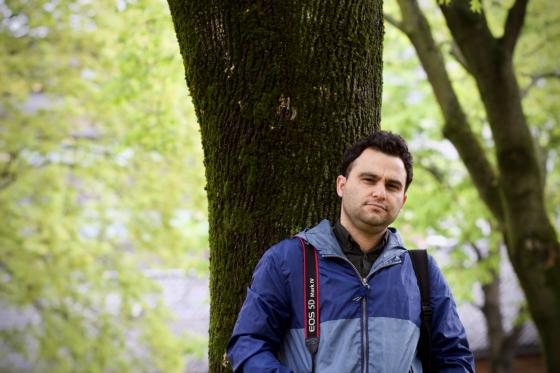 Javad Parsa med et kamera hengende over skulderen. Gr&oslash;nne tr&aelig;r i bakgrunnen.