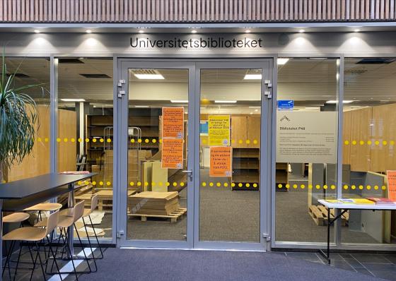 Bildet viser utsiden av biblioteket p&aring; P48. Her ser man det henger flere plakater, som handler om at oppussingen kommer til &aring; vare ut februar, og hvor man kan finne hjelp. Igjennom vinduet kan man se at det fortsatt arbeides med montering.