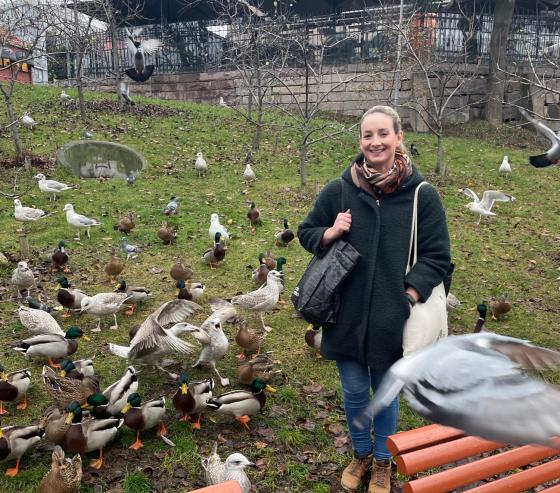 Mai Amundsen st&aring;r og smiler til kameraet. Rundt henne g&aring;r det en haug med ulike fugler, blant annet m&aring;ker og ender.