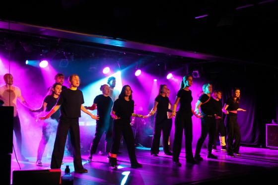 Skuespillere st&aring;r p&aring; en scene i rosa lys under et sangnummer.