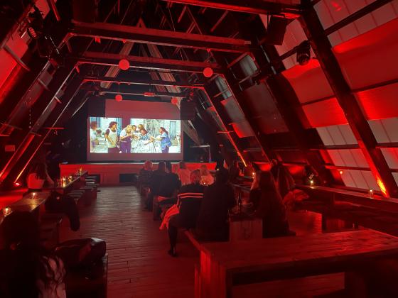 Et rom med r&oslash;de lys, og en storskjerm som viser filmen Mamma Mia 