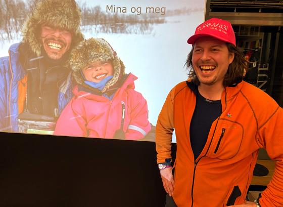 Alexander Read fra Mina og Meg st&aring;r foran skjerm med bilde av han og Mina