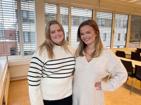 Ingerid Bernhoft (25) og Anea Sorthe (23) smiler til kameraet i et av OsloMet sine klasserom. 