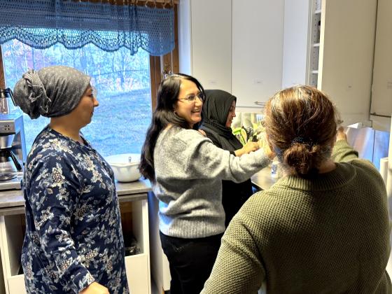 Fire damer som st&aring;r trangt p&aring; et lite kj&oslash;kken og lager mat mens de smiler og ler