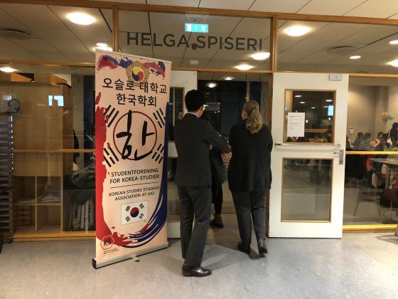 Tre personer g&aring;r inn d&oslash;ren til en kafeteria. Ved siden av er banneret til Korean Studies Student Association