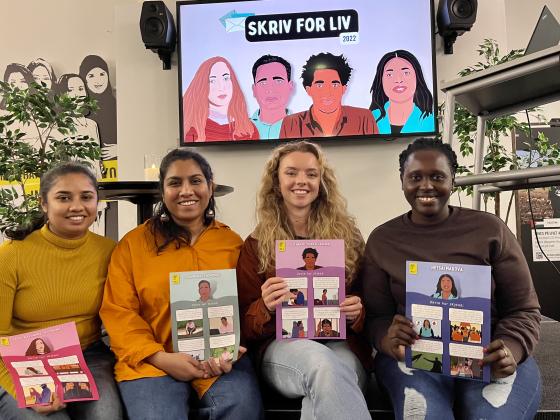 Fire unge kvinner sitter p&aring; en scene og viser frem plakater