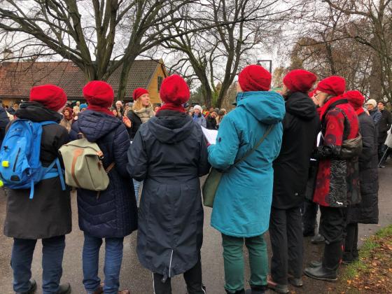 Koret har r&oslash;de luer og synger foran publikum