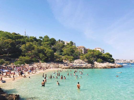 P&aring; bildet ser man mennesker som ligger p&aring; stranda. Sola skinner og vannet er turkist. Foto Lauren Hannah. 