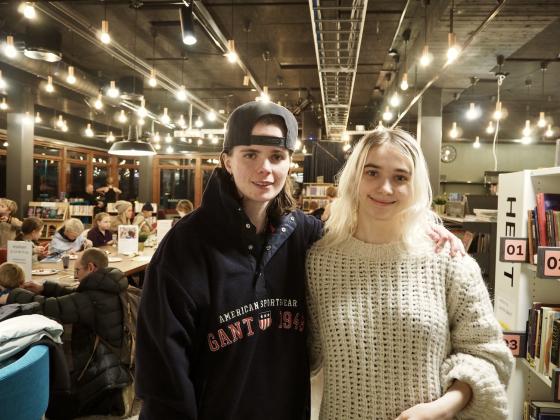 To jenter st&aring;r foran bord med barn som maler