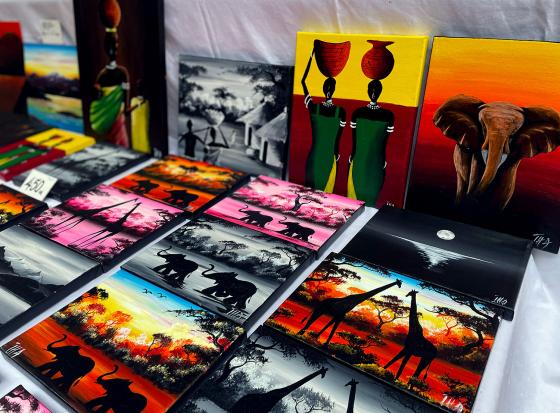 Bildet viser flere malerier utstilt p&aring; et bord under s&oslash;ndagsmarked. Mange av bildene inneholder dyr. 