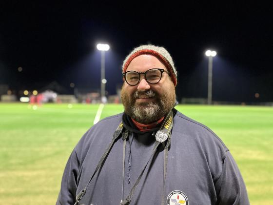 Marius Helg&aring; smiler til kamera, med en fotballbane i bakgrunnen.