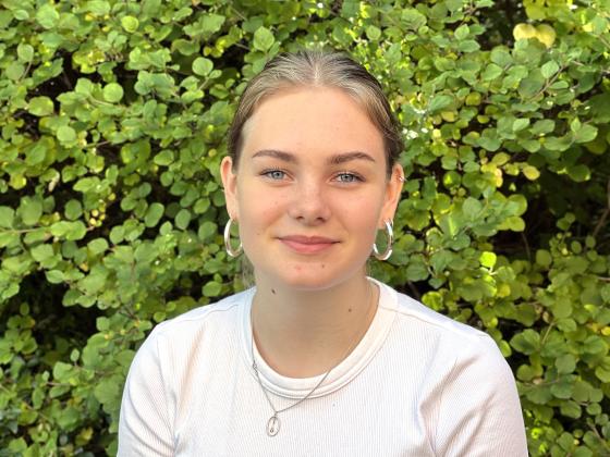 Portrettbilde av Martine Svendsen som smiler med en gr&oslash;nn busk