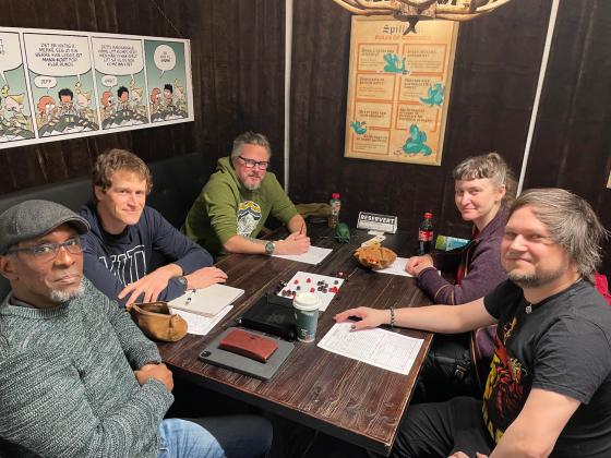 Fem mennesker som sitter rundt et bord og spiller rollespillet Vampire the Masquerade. P&aring; bordet ligger det terninger og ark med rollebeskrivelser.