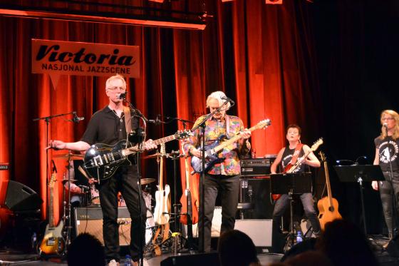 Bandet st&aring;r p&aring; scenen. Sigmund &Oslash;vrum synger mens Dag Vargseth spiller gitar. Rundt dem ser man de andre bandmedlemmene. 
