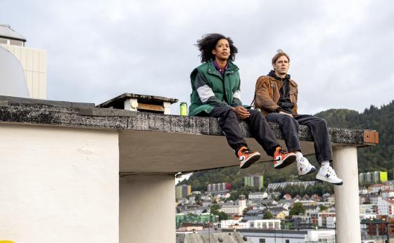 Hovedrollene Odilie og Stian sitter p&aring; et tak og ser utover Bergen by
