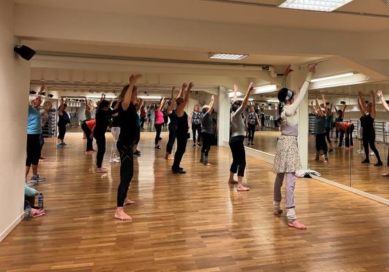 Bildet viser et rom med store speil, med en stor gruppe eldre kvinner som holder armene i v&aelig;ret under en trenings&oslash;kt. 