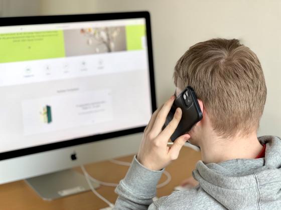 Person sitter med telefonen mot &oslash;re og ser p&aring; PCen. 