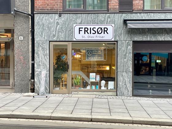 Bildet viser inngangen til St. Olav Fris&oslash;r i St. Olavs Gate i Oslo. I vinduet til salongen ser man planter, h&aring;rprodukter og et skilt med telefonnummeret til salongen og informasjon om studentrabatt.