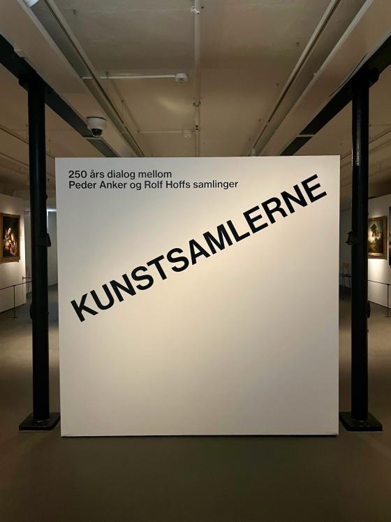 Bildet viser inngangspartiet til kunstutstillingen p&aring; Bogstad g&aring;rd. Den heter Kunstsamlerne, og navnet er skrevet i svarte blokkbokstaver p&aring; et hvitt lerret. 