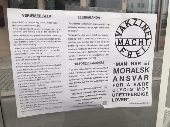 Plakat der det st&aring;r "Vakzine Macht Frei"