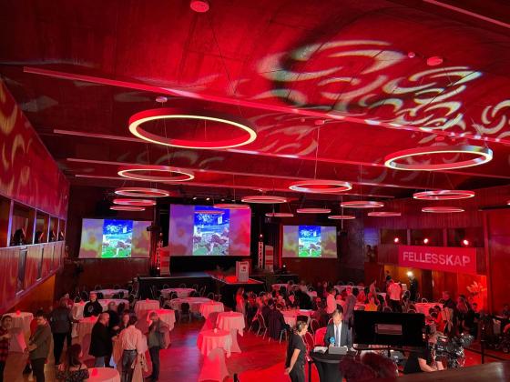 stor gruppe med mennesker er samlet i et lokale som er lyst opp av r&oslash;dt lys