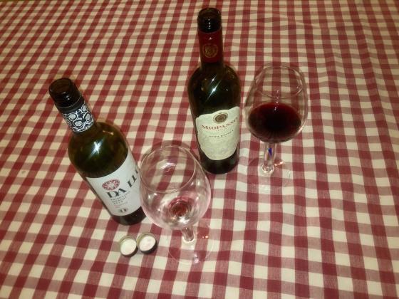 To flasker, og et glass som st&aring;r p&aring; et bord med r&oslash;dt og hvit rutete duk