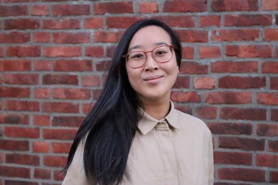 Xueqi Pang ser inn i kameraet foran en r&oslash;d murvegg