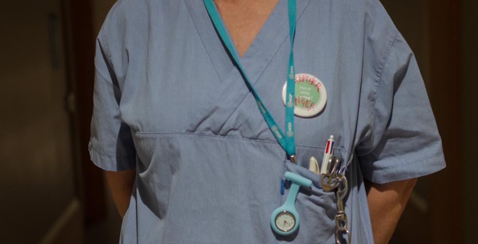 n&aelig;rbilde av sykepleieruniform, den er bl&aring; og har en klokke i lomma og en navnetag