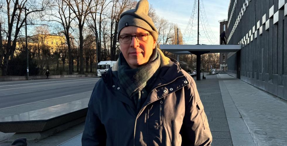 Ola Manns&aring;ker utenfor den gamle amerikanske ambassaden med sidelys fra morgensolen. Har p&aring; ytterkl&aelig;r: lue, skjerf og tykk jakke. Seri&oslash;st ansiktsuttrykk. 