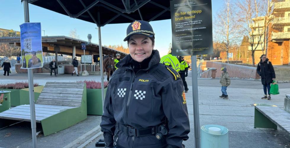 Politibetjent st&aring;r foran en stand p&aring; Mortensrudtorget og smiler