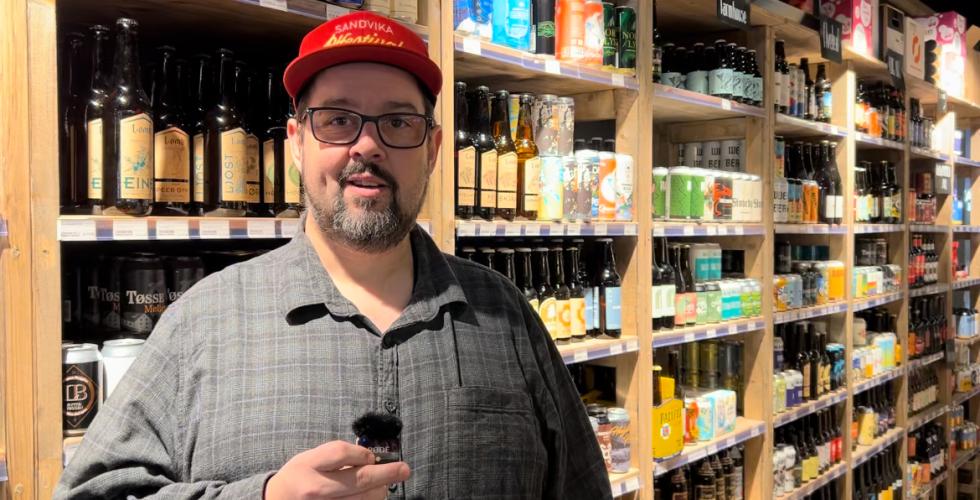 Mann foran en hylle med &oslash;l if&oslash;rt caps.