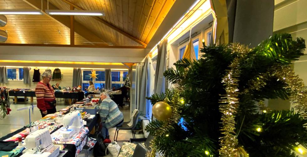 Et juletre med en hvit stjerne i front, og et lokale med eldre damer som selger husflidsvarer i bakgrunnen