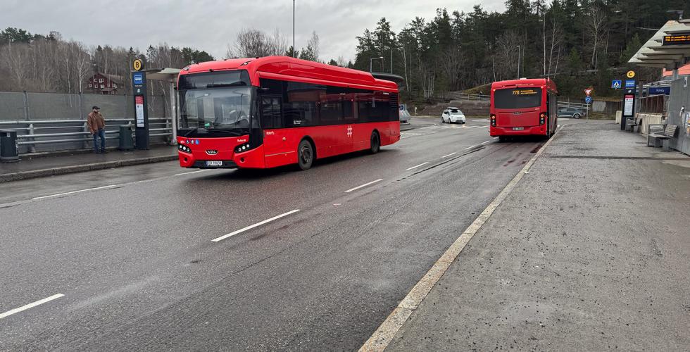 Det er to r&oslash;de ruter-busser p&aring; holdeplassen.