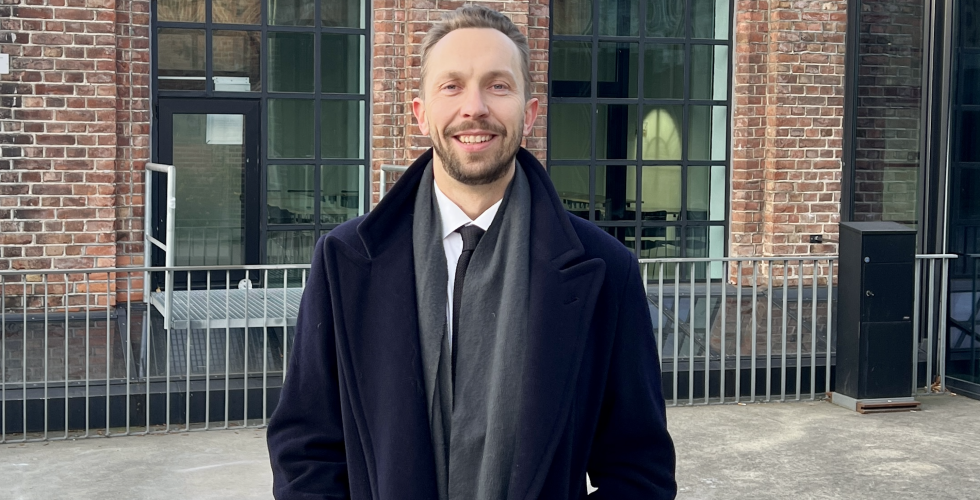 Mann i frakk smiler foran Kunsth&oslash;gskolen i Oslo