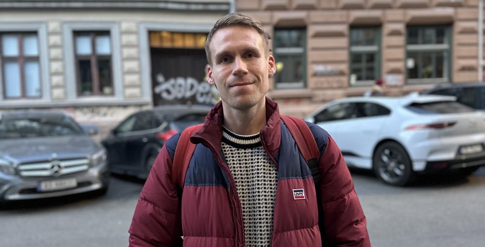 Mann st&aring;r i gata og smiler til kamera. Han har p&aring; islender og r&oslash;d boblejakke. 