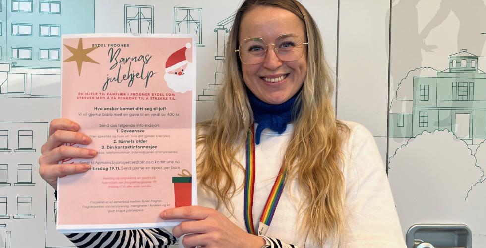 Hege Fr&oslash;ystad holder opp plakaten til "Barnas Julehjelp" mens hun smiler til kameraet