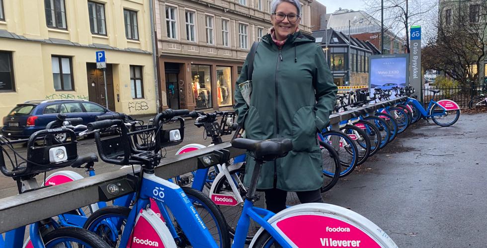 En dame st&aring;r ved masse sykler og smiler.