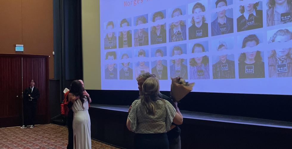 Mennesker klemmer hverandre i en kinosal, med blomster i h&aring;nda