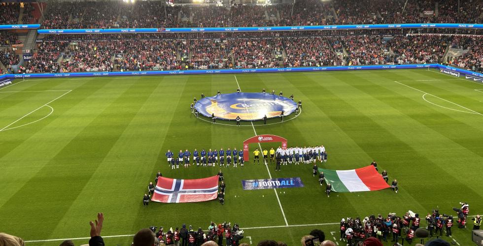 Spillerne synger nasjonalsangen med flaggene foran seg.