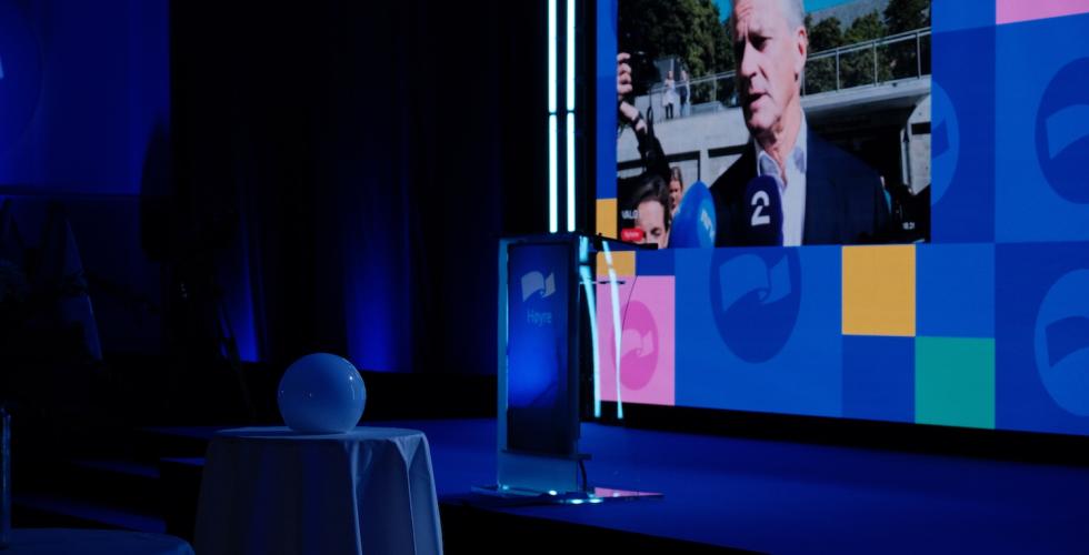 Talerstolen plassert midt p&aring; scenen, med Jonas Gahr St&oslash;re p&aring; skjermen i bakgrunnen