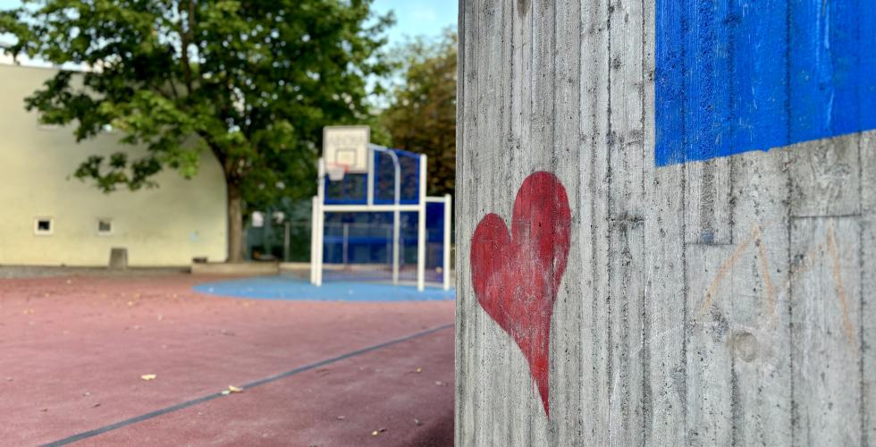 Et hjerte p&aring; en vegg, med en basketball bane i bakgrunnen i en skoleg&aring;rd