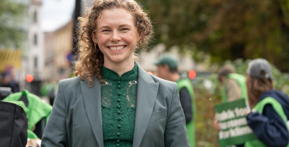 En dame, med MDG representater if&oslash;rt gr&oslash;nne vester i bakgrunnen