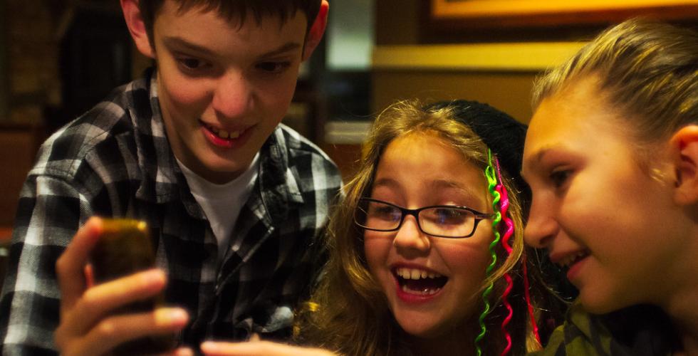 Tre barn ser p&aring; en mobil og smiler 