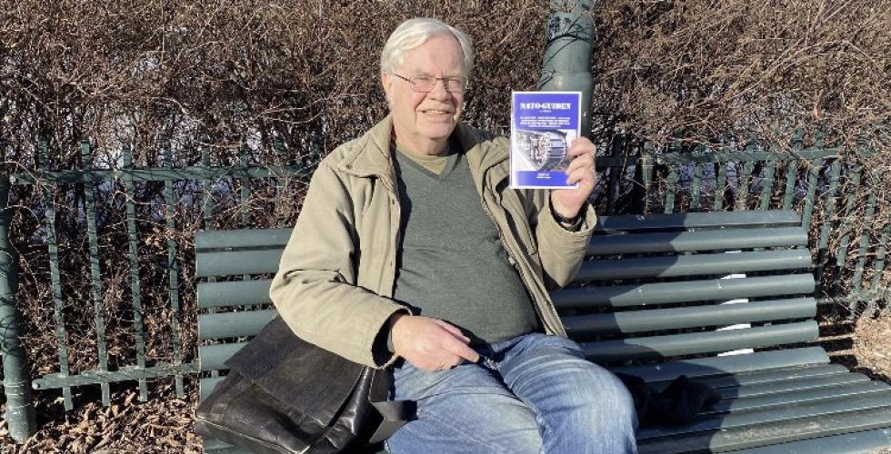 Geir Hem sitter p&aring; en benk med en brosjyre i h&aring;nda.