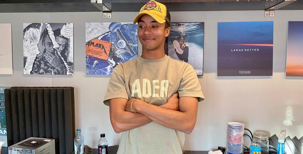 Artist Adrian Amara st&aring;r foran en vegg i studioet sitt med bilder av tidligere album han har laget. 