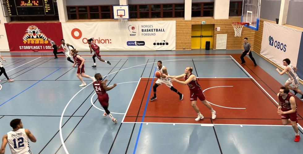 Spillere p&aring; en basketball bane som springer mot ballen. 