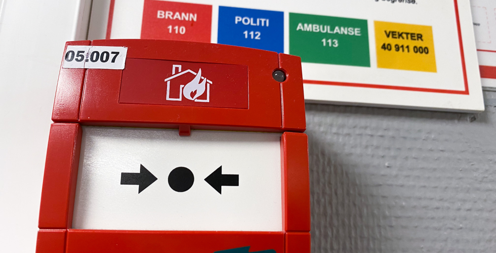 Bilde av en r&oslash;d brannvarsler med n&oslash;dnummerene bak. Bildet er tatt p&aring; OsloMet