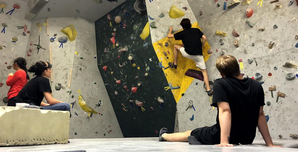 En person klatrer i en klatrevegg mens andre ser p&aring;